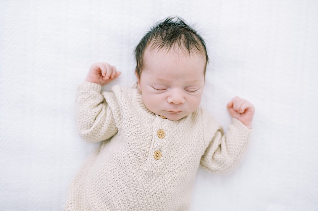 Newborn baby boy wearing beige sweater laying on white bedding portrait image by Portland Newborn and Maternity Family Photographer Emilie Phillipson Photography. 