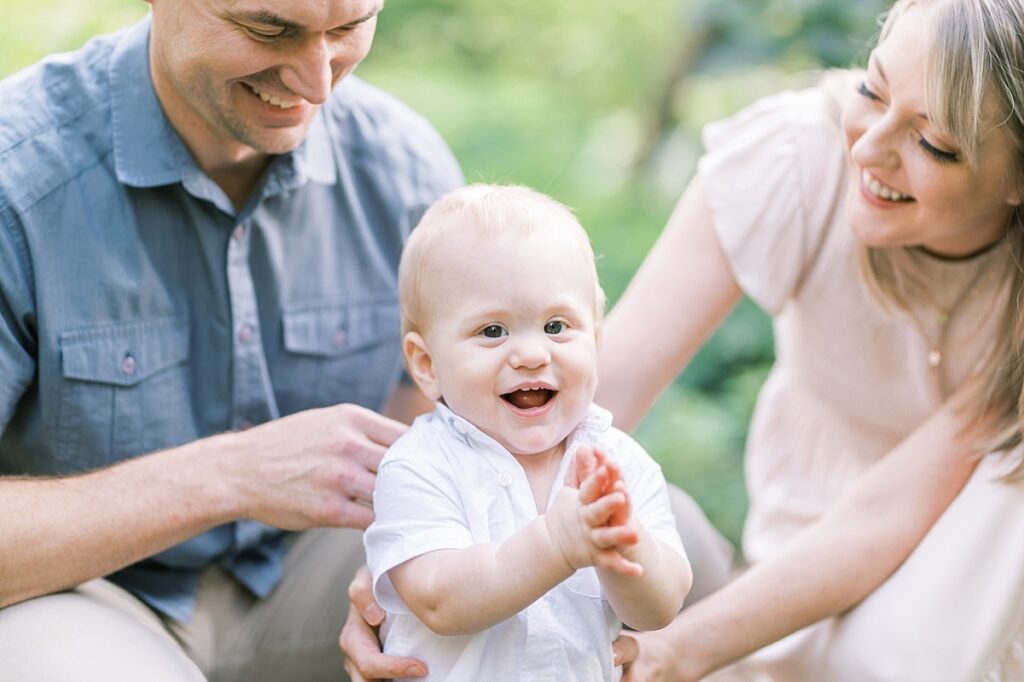 Image of two parents looking at child while child smiles and claps at the camera image by Portland Family Photographer Emilie Phillipson Photography. 