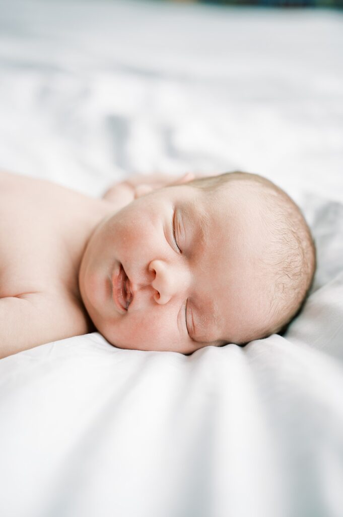 Image of newborn baby face and top of shoulders laying asleep on white bedding by Portland Newborn Photographer Emilie Phillipson Photography