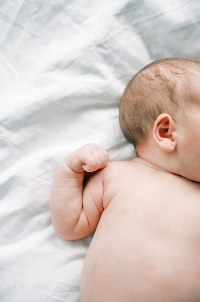 Image of baby hands curled up and back of head and ear showing laying on white bedding by Portland Newborn Photographer Emilie Phillipson Photography