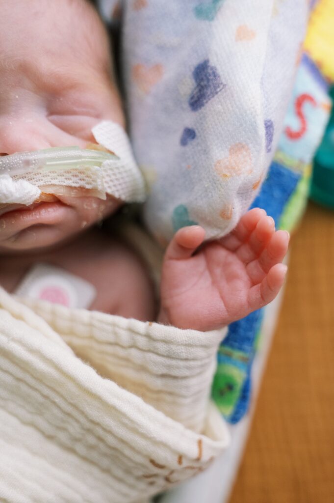 Close up image of premature baby face with nasal cannula and very small hand wrapped in swaddle by Portland NICU photographer Emilie Phillipson Photographer