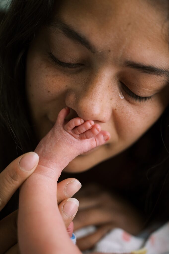 Woman kissing small baby foot with tear on her eye by Portland NICU and family photographer Emilie Phillipson Photography